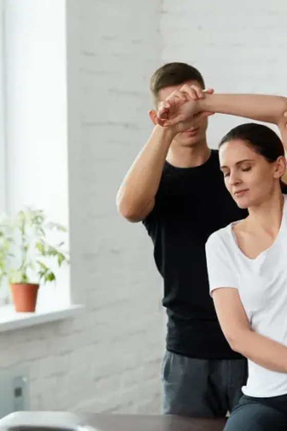 Therapist guiding a seated patient through an overhead shoulder movement