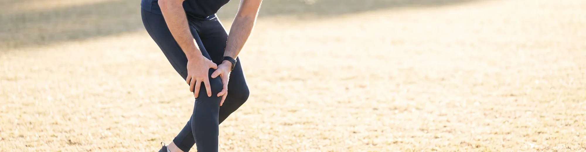 Athlete outdoors gripping his knee in pain during a workout
